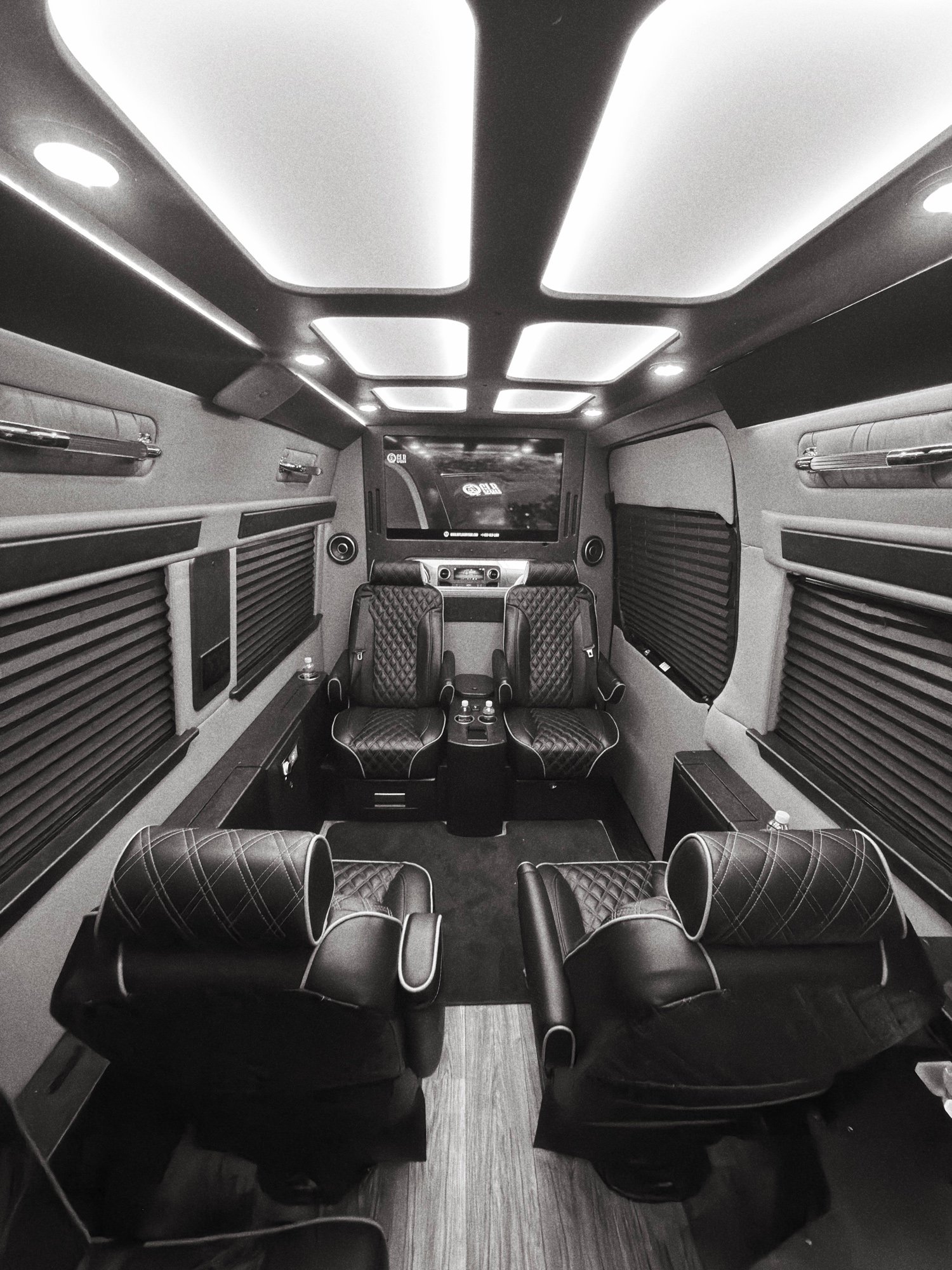 Executive Mercedes-Benz Sprinter interior with diamond-stitched captain's chairs, 4K conference screens, workstation lighting